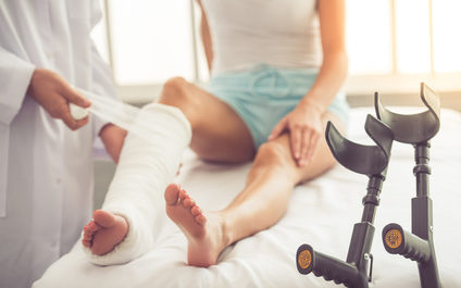 Doctor and patient Cropped image of handsome doctor bandaging woman's broken leg while working in his office